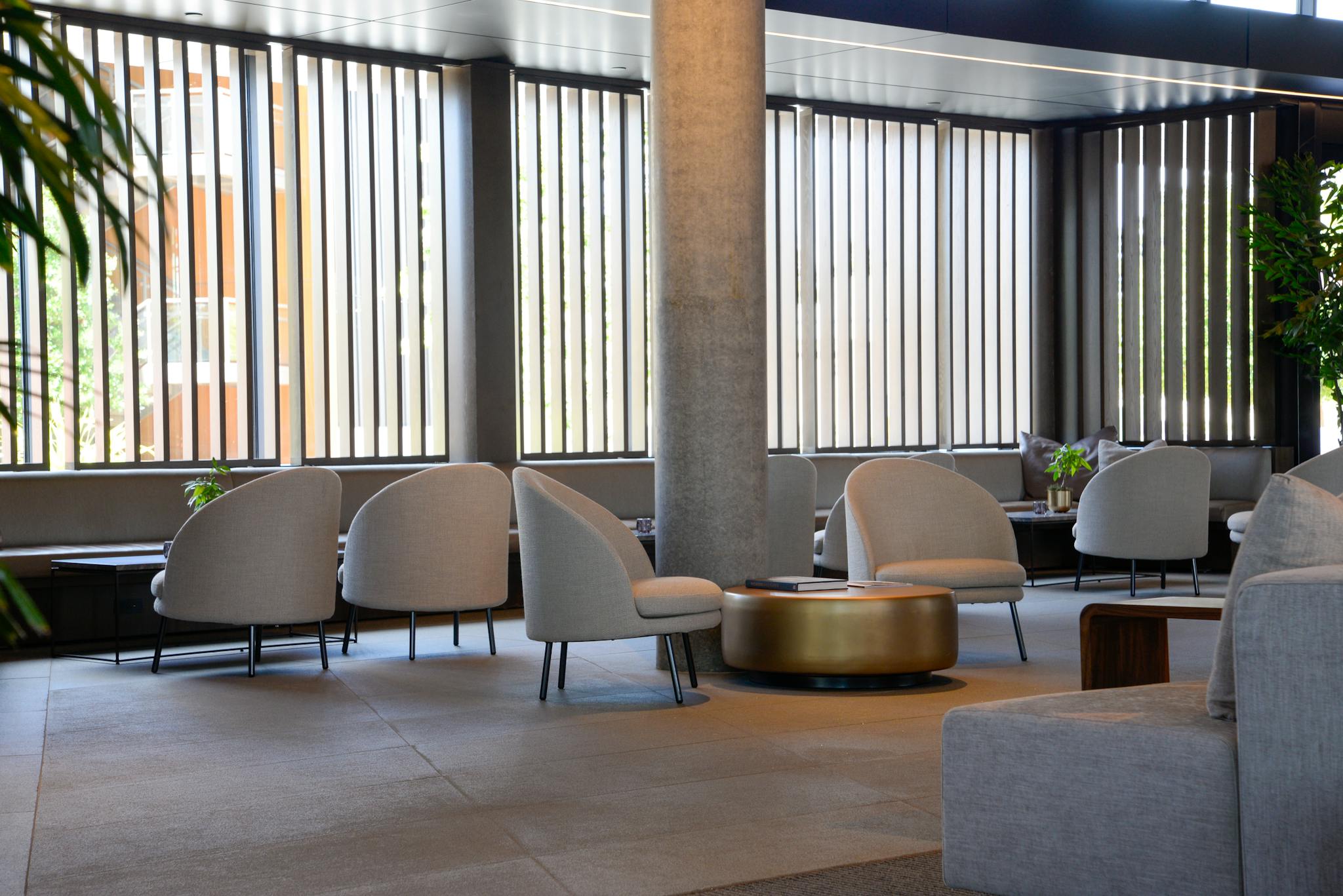 Spacious hotel lounge with stylish chairs and tables, featuring natural light and modern design elements.